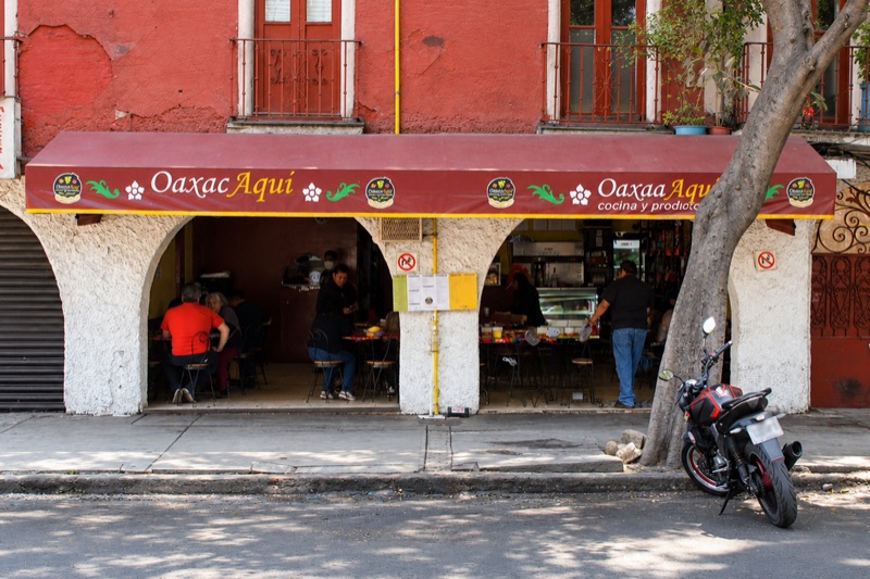 Oaxacaquí’s storefront in Santa María la Ribera: maroon awning with the logo, white arches and people eating at the tables